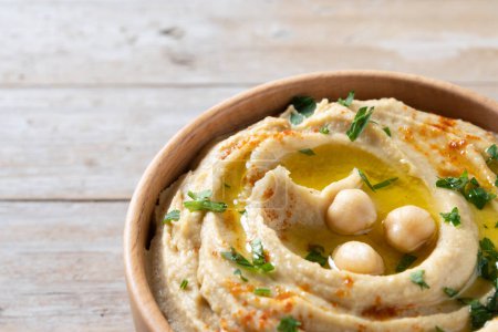 Téléchargez les photos : Hummus de pois chiches dans un bol en bois garni de persil, paprika et huile d'olive sur une table en bois. Espace de copie - en image libre de droit