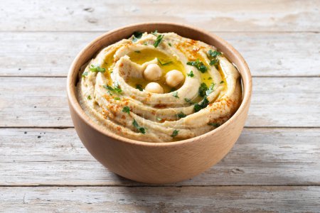 Photo for Chickpea hummus in a wooden bowl garnished with parsley, paprika and olive oil on wooden table - Royalty Free Image