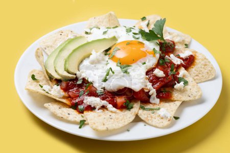 Traditionelles mexikanisches Frühstück rote Chilaquiles mit Ei auf gelbem Hintergrund