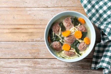 Italian Wedding Soup with meatballs and spinach on wooden table. Top view. Copy space