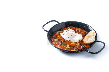 Vegetable pisto manchego with tomatoes, zucchini, peppers, onions,eggplant and egg, served in frying pan isolated on white background. Copy space