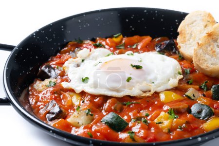 Vegetable pisto manchego with tomatoes, zucchini, peppers, onions,eggplant and egg, served in frying pan isolated on white background