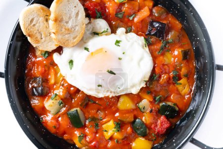 Gemüse Pisto Manchego mit Tomaten, Zucchini, Paprika, Zwiebeln, Auberginen und Ei, serviert in der Pfanne isoliert auf weißem Hintergrund. Nahaufnahme