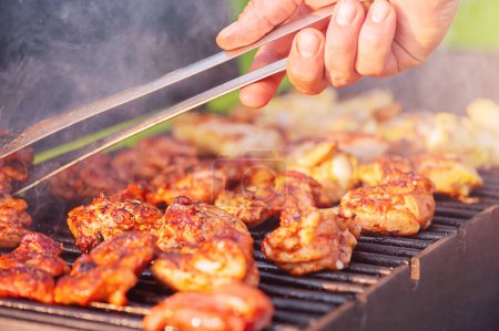 Photo for Cooking chicken wings on the fire. Picnic, street food. A man's hand flips wings on a grill. - Royalty Free Image