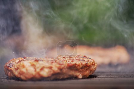 Photo for Street food, cooking meat. A very narrow focal point on a patty being grilled at a picnic. - Royalty Free Image