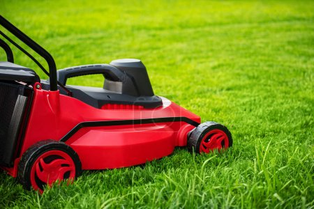Photo for Red and black lawnmower on green grass. The process of mowing the lawn with a lawnmower. - Royalty Free Image