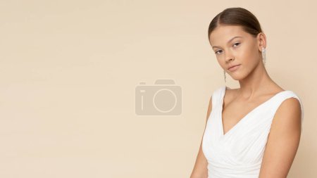 Téléchargez les photos : Jeune femme pose en robe de mariée blanche sur fond brun clair isolé. - en image libre de droit