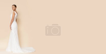 Téléchargez les photos : Jeune femme pose en robe de mariée blanche sur fond brun clair isolé. - en image libre de droit