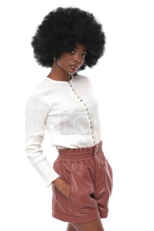 Foto de Hermosa modelo de moda africana en camisa blanca y pantalones cortos de cuero sobre fondo blanco aislado. - Imagen libre de derechos