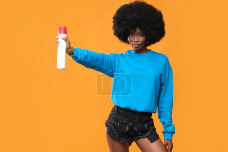 Téléchargez les photos : Modèle à la peau noire avec une coiffure afro et peinture en aérosol à la main sur un fond orange. - en image libre de droit