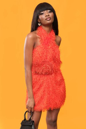 Téléchargez les photos : Brune très à la mode en robe rouge et talons hauts sur fond orange. - en image libre de droit