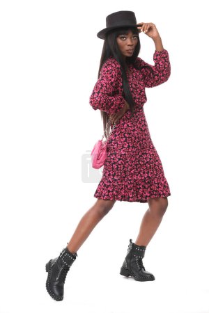 Foto de Modelo femenino de moda con vestido floral, sombrero, bolso y zapatos de cuero sobre fondo blanco aislado. - Imagen libre de derechos
