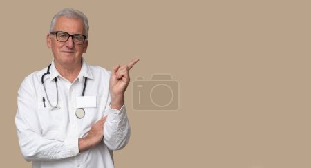 Médico mayor en gafas graduadas con estetoscopio y uniforme blanco sobre fondo marrón claro.