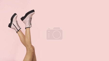 Foto de Las botas a la moda rosadas sobre las piernas delgadas femeninas sobre el fondo de color rosa pastel con el lugar libre para el texto. - Imagen libre de derechos