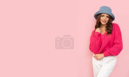 Foto de Elegante morena sonriente en sombrero azul y suéter sobre fondo rosa pastel con lugar para texto. - Imagen libre de derechos