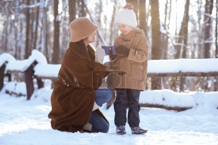 Foto de Mamá e hijo tienen un descanso de té de invierno en la hermosa zona de bosque nevado. - Imagen libre de derechos