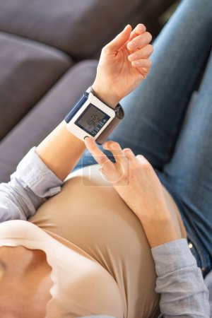 Foto de A pregnant woman digests the results on a blood pressure monitor. - Imagen libre de derechos