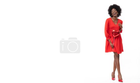 Foto de Lindo modelo femenino africano con vestido rojo y corazón en forma de globo en la mano sobre fondo blanco aislado. - Imagen libre de derechos