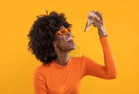 Foto de Mujer africana feliz con rebanada de pizza sobre fondo amarillo aislado. - Imagen libre de derechos