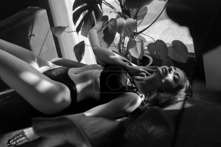 Photo for A very attractive brunette in black lingerie is lying on a gray sofa. The perfect play of light and shadow in a black and white photo. - Royalty Free Image