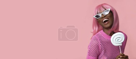 Foto de Lindo modelo femenino con pelos rosados y piruleta sobre fondo rosa pastel aislado. - Imagen libre de derechos