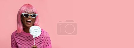Foto de Lindo modelo femenino con pelos rosados y piruleta sobre fondo rosa pastel aislado. - Imagen libre de derechos