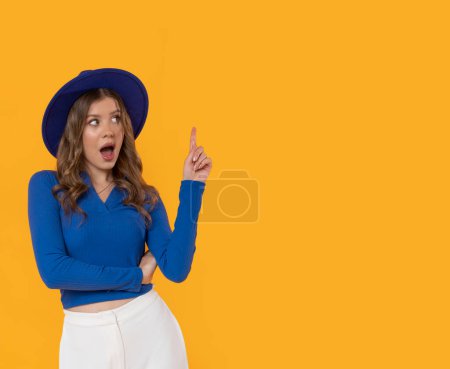 Téléchargez les photos : Une jeune femme folle dans un chapeau bleu et chemisier sur un fond jaune avec de l'espace pour le texte. - en image libre de droit