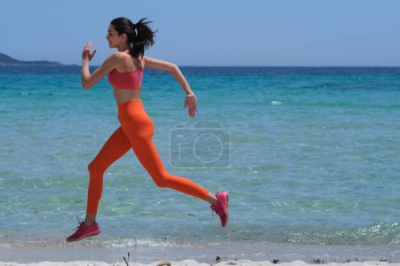 Photo for A beautiful brunette is jogging on the beach in sports clothes. - Royalty Free Image