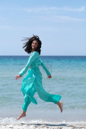 Foto de Hermosa morena en ropa turquesa en la playa. - Imagen libre de derechos