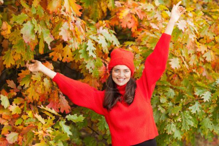 Photo for Beautiful brunette in an autumn scenery with a red hat and scarf. - Royalty Free Image