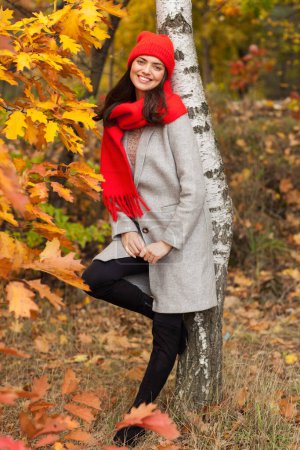 Photo for Beautiful brunette in an autumn scenery with a red hat and scarf. - Royalty Free Image