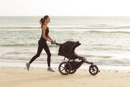 Téléchargez les photos : Maman sportive avec une poussette court sur la plage. - en image libre de droit