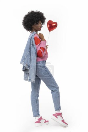 Téléchargez les photos : Heureuse femme noire avec des cheveux afro et tenue en denim tient coeur de ballon sur fond blanc isolé. - en image libre de droit