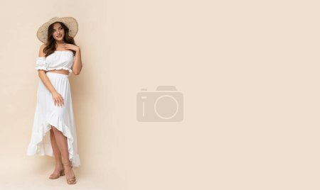 Foto de Mujer joven muy hermosa en sombrero de paja y vestido boho blanco sobre fondo cremoso. - Imagen libre de derechos