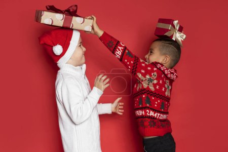 Foto de Dos chicos se divierten con regalos de Navidad sobre fondo rojo. - Imagen libre de derechos