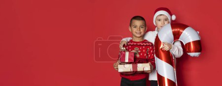 Téléchargez les photos : Deux garçons s'amusent avec des cadeaux de Noël sur fond rouge. - en image libre de droit