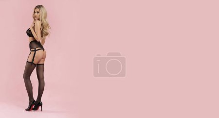 Téléchargez les photos : Blonde parfaite en lingerie noire sur fond rose isolé. - en image libre de droit