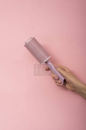 Foto de Rodillo de polvo en la mano de una mujer sobre un fondo rosa. - Imagen libre de derechos