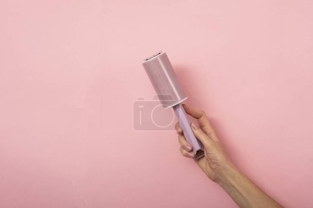 Foto de Rodillo de polvo en la mano de una mujer sobre un fondo rosa. - Imagen libre de derechos