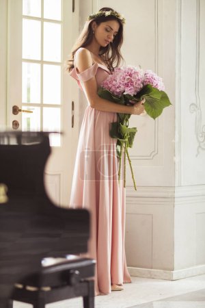 Téléchargez les photos : Belle femme dans une robe longue avec un bouquet de fleurs dans un palais intérieur. - en image libre de droit
