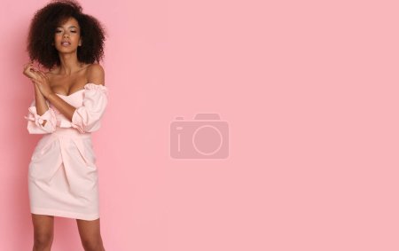 Foto de Hermosa mujer afroamericana en un vestido rosa sobre un fondo rosa. - Imagen libre de derechos