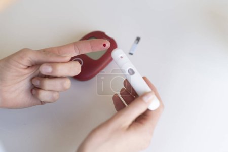 Photo for A young woman measures her blood sugar level using aglucometer. - Royalty Free Image