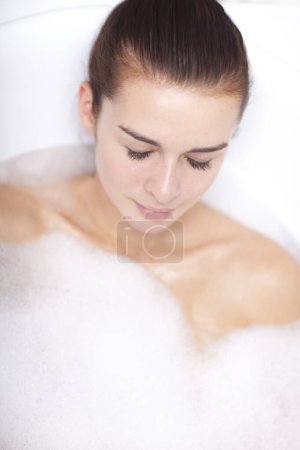 Téléchargez les photos : Une jeune femme prend un bain dans une baignoire pleine de mousse. - en image libre de droit