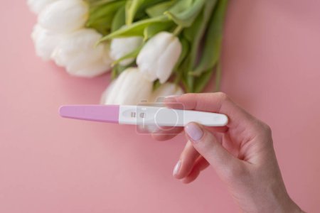 Téléchargez les photos : Test de grossesse positif dans la main d'une femme sur un fond rose pastel. - en image libre de droit