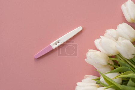 Téléchargez les photos : Test de grossesse positif dans la main d'une femme sur un fond rose pastel. - en image libre de droit