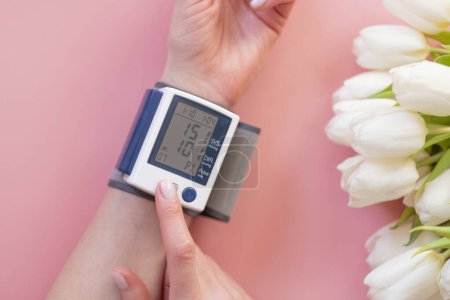 Foto de Las manos femeninas y un monitor de presión arterial con flores sobre un fondo rosa. - Imagen libre de derechos