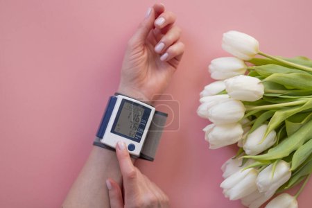 Foto de Las manos femeninas y un monitor de presión arterial con flores sobre un fondo rosa. - Imagen libre de derechos