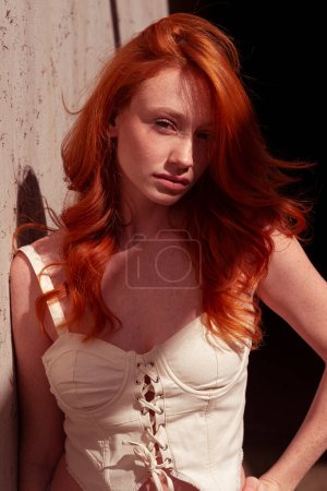 Téléchargez les photos : Belle fille aux cheveux roux avec des taches de rousseur dans une tenue à la mode sur un mur gris. - en image libre de droit