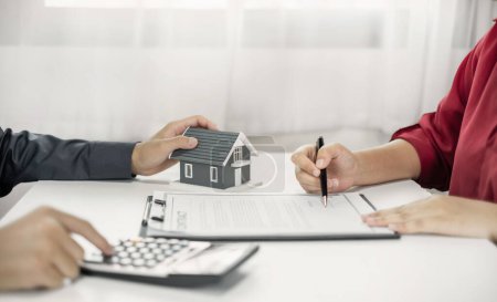 Téléchargez les photos : Un agent immobilier avec un modèle de maison discute avec les clients de la location d'une maison, de l'achat d'une assurance habitation et de la conclusion du contrat après la négociation officielle.. - en image libre de droit