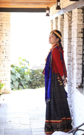una chica aldeana vestida con vestimenta tradicional Gurung camina por la escalera y mira la cámara 